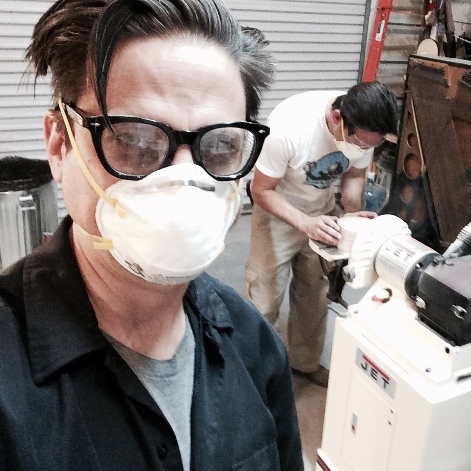 Two people wearing protective masks working with a woodworking machine in a workshop.