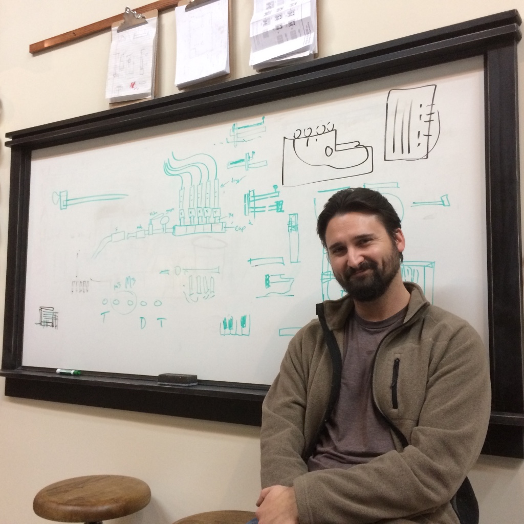 Person seated in front of a whiteboard with hand-drawn technical diagrams.